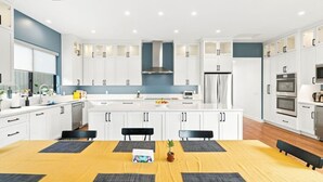 A modern kitchen with white cabinetry, a central island, and built-in appliances. - Sunny Palms Luxury Home - Northpark (San Diego)