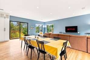 Ein modernes Wohnzimmer mit Essbereich, einer Sofagarnitur, einem Fernseher und Blick ins Freie.