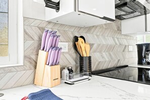 A modern kitchen with a herringbone tile backsplash, a knife block, a coffee maker, and a countertop. - Brand New Condo Near Downtown, Coronado (San Diego)