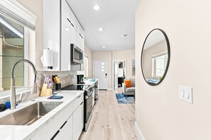 A modern kitchen with white cabinets, a stainless steel sink, and a microwave. - Brand New Condo Near Downtown, Coronado (San Diego)