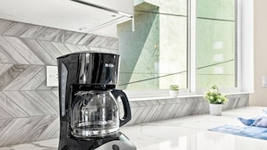 A modern coffee maker on a kitchen counter with a herringbone-patterned backsplash and a window with a view of greenery. - New 2BR Home Minutes to Downtown SD (San Diego)
