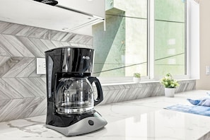 A modern coffee maker on a kitchen counter with a herringbone-patterned backsplash and a window with a view of greenery. - New 2BR Home Minutes to Downtown SD (San Diego)