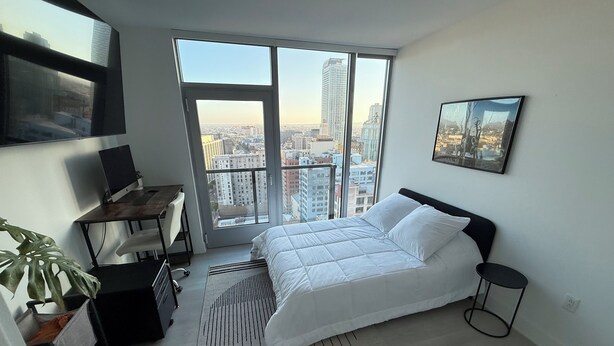 Ein modernes Schlafzimmer mit großem Fenster, einem Bett, einem Schreibtisch und einem Stuhl.
