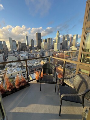 A balcony with two wicker chairs, a glass railing, and a cityscape view. - Bedroom in penthouse downtown Los Angeles (Los Angeles)