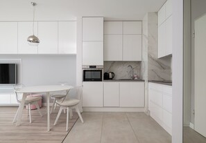 A modern kitchen with white cabinetry, a built-in oven, a stainless steel sink, and a dining area with a white table and chairs. - Business Mokotów Park 15 Apartment (Warszawa)
