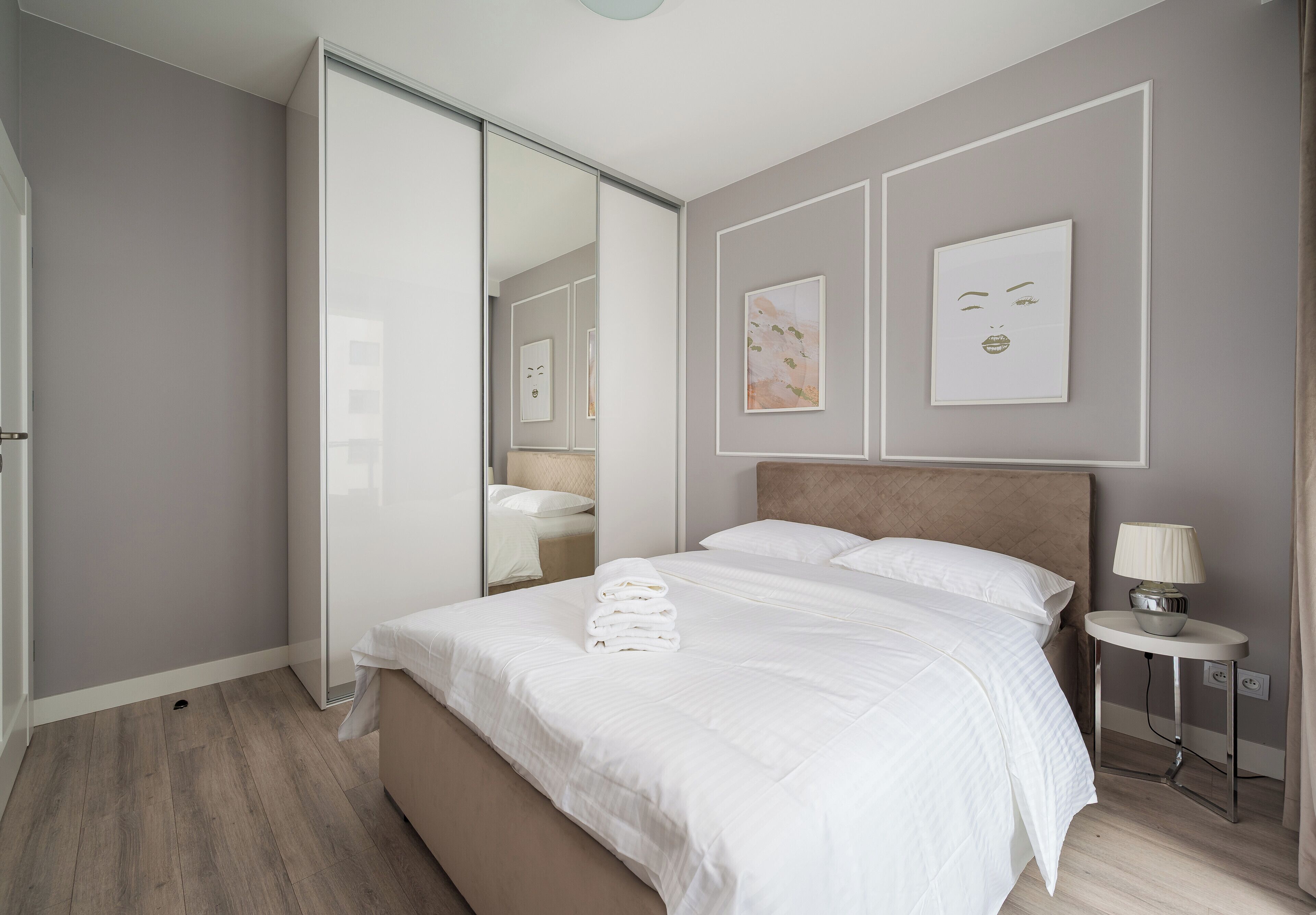 A modern bedroom with a large bed, a bedside table with a lamp, and artwork on the walls.