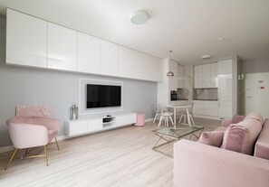 Ein modernes Wohnzimmer mit Flachbildfernseher, weißen Schränken, einem Glastisch und rosa Möbeln.