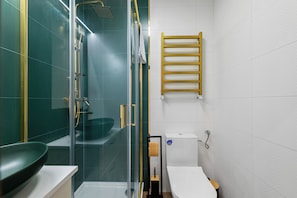 A modern bathroom with a glass shower enclosure, a wooden towel rack, and a toilet. - Cyrulicza Old Town Apartment (Lublin)