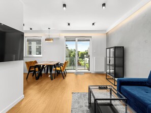 A modern living room with a dining area, a sofa, a glass coffee table, and a view of the outdoors. - Krowodrza Superior Apartment (Kraków)