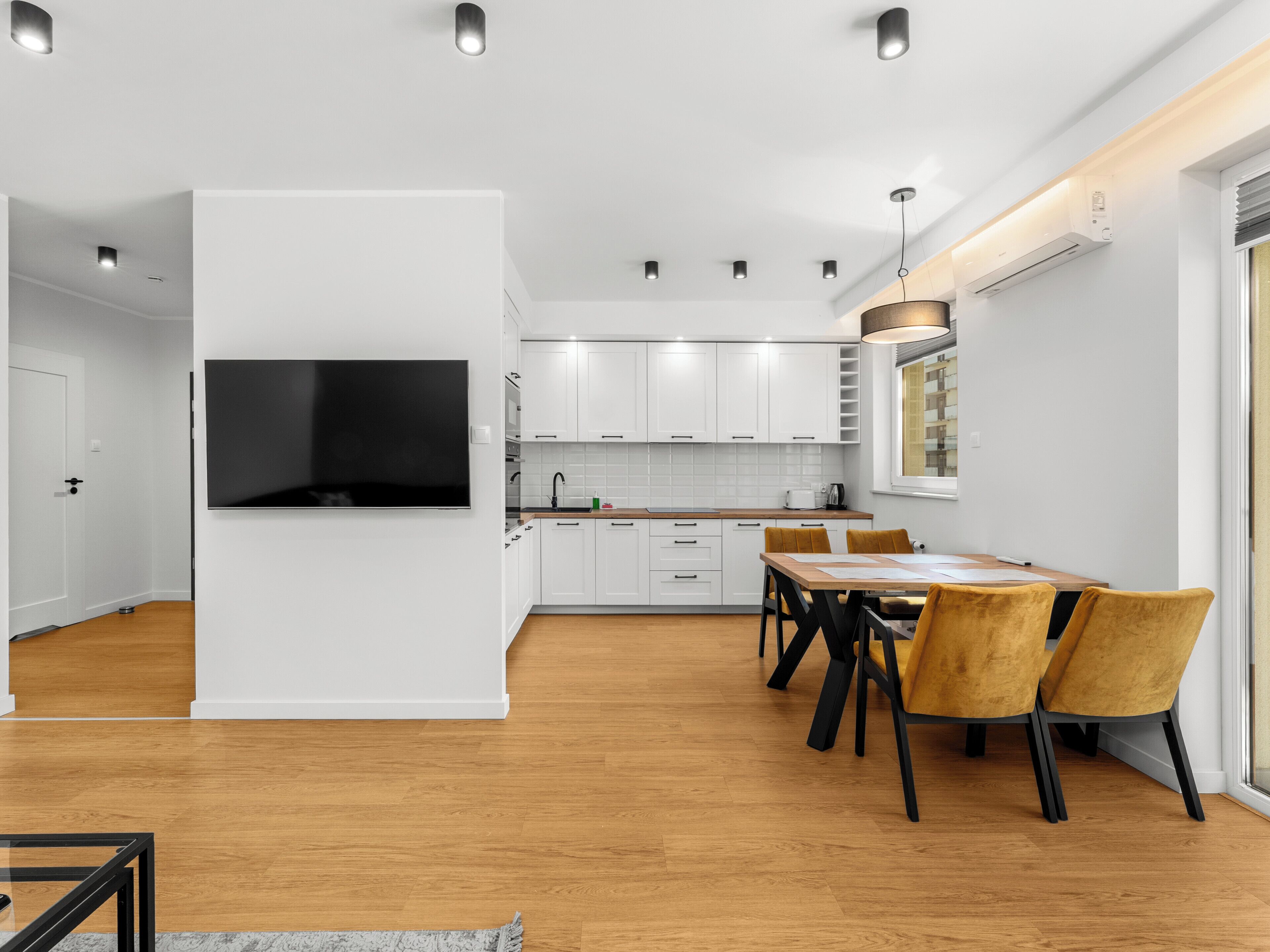 Eine moderne Küche mit weißen Schränken, einem Flachbildfernseher und einer Essecke mit Holzkästen.