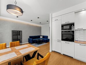 A modern kitchen with white cabinets, a Bosch oven, and a dining area with a wooden table and yellow chairs. - Krowodrza Superior Apartment (Kraków)