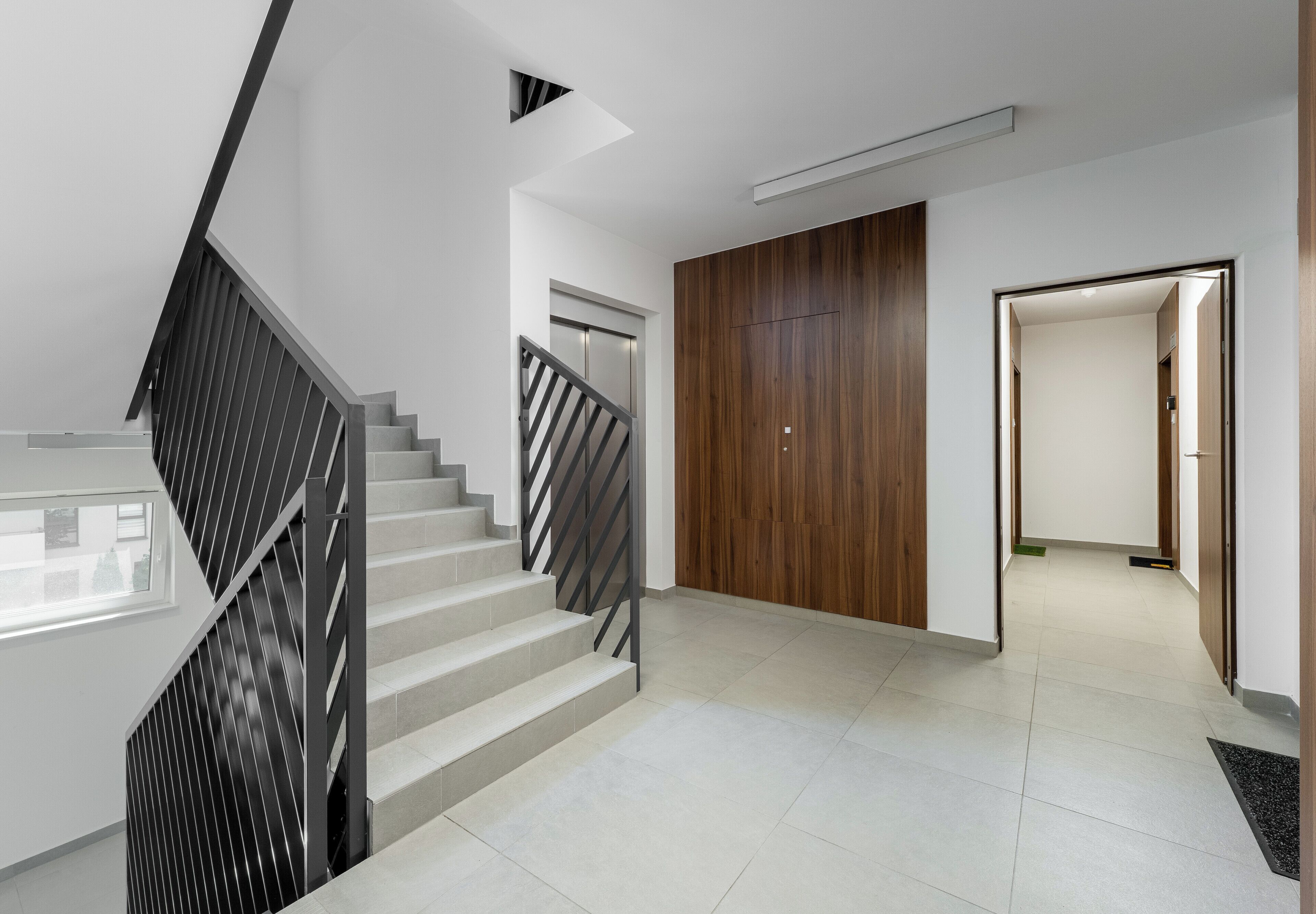 A modern interior with a staircase, a wooden door, and a hallway leading to another room.
