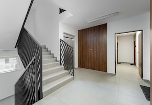 A modern interior with a staircase, a wooden door, and a hallway leading to another room. - Krowodrza Superior Apartment (Kraków)