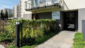 En modern byggnad med en balkong, en skylt som visar adressen och ett välskött trädgårdsområde.