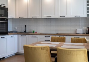 A modern kitchen with white cabinets, a wooden countertop, and a dining table with chairs. - Krowodrza Superior Apartment (Kraków)