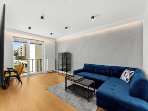 A modern living room with a blue sofa, a glass coffee table, and a view of the outside. - Krowodrza Superior Apartment (Kraków)