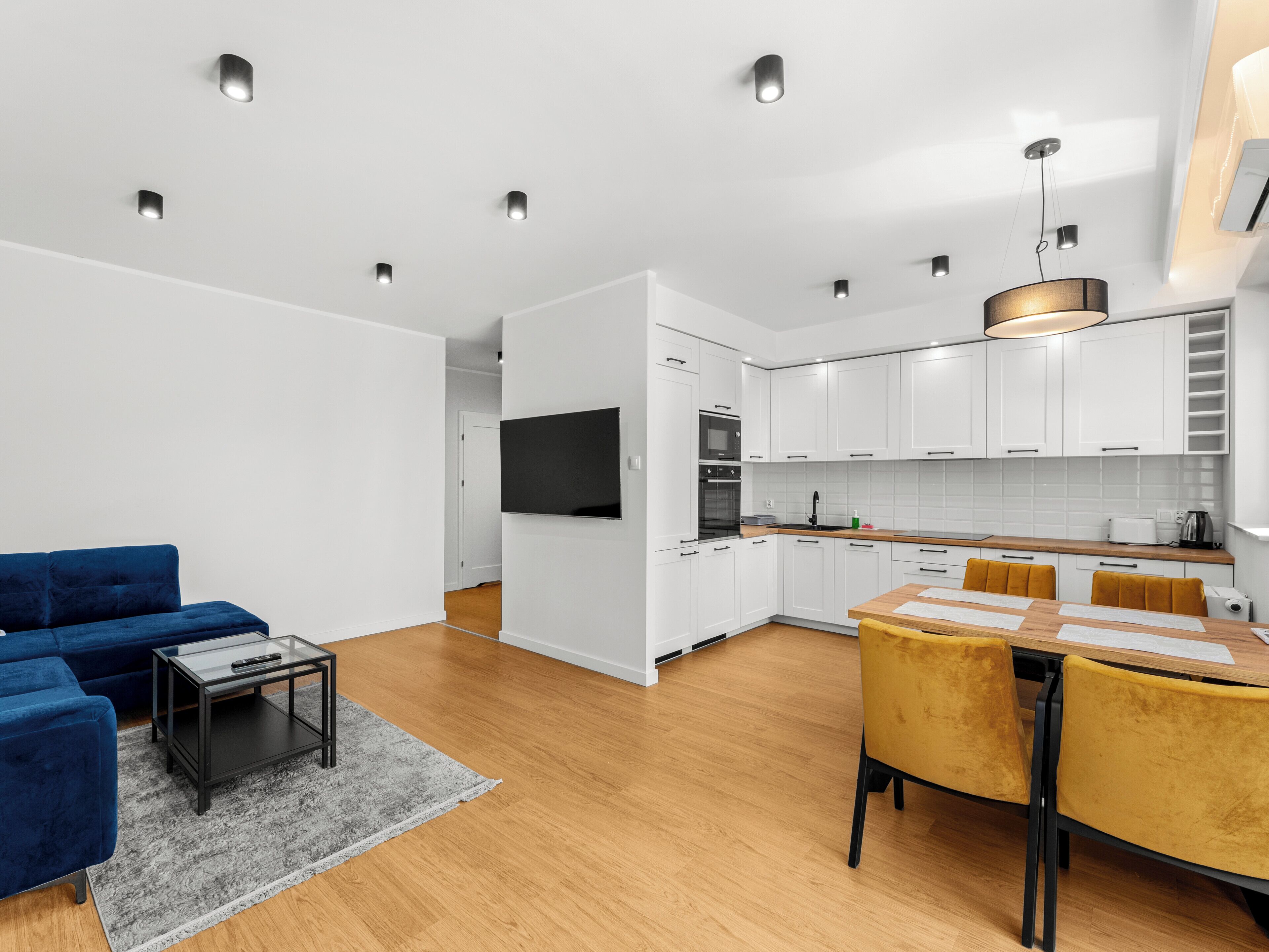 A modern living room with a blue sofa, a coffee table, and a TV mounted on the wall.