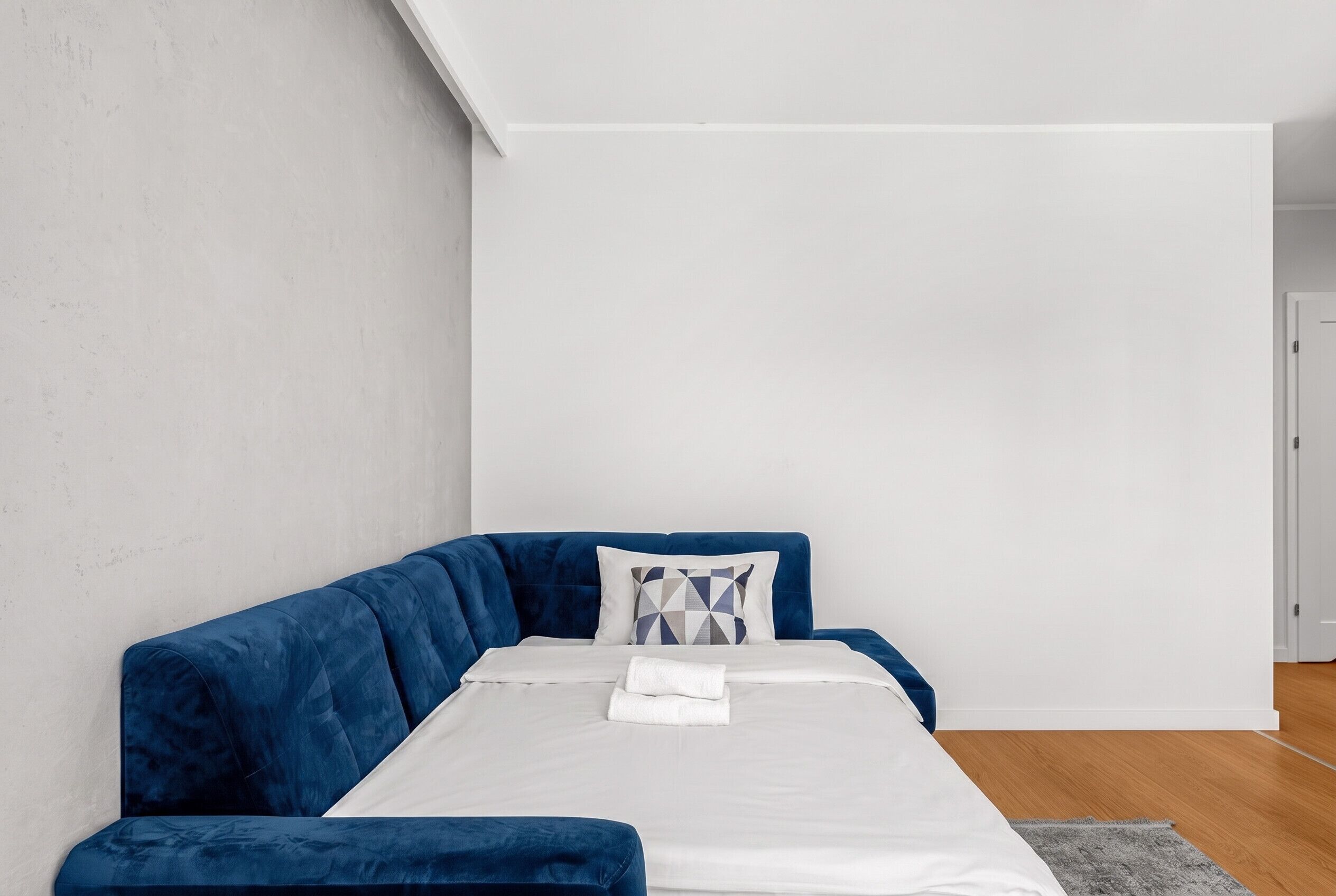 A modern room with a blue sectional sofa, a white bed, and a gray rug.