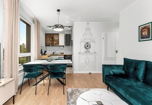 A modern living room with a teal sofa, a dining area with a white table, and a kitchen with wooden cabinets. - Portowa Riverside Apartment (Kraków)