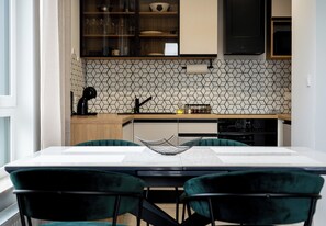 A modern kitchen with a geometric backsplash, wooden cabinets, and a dining area with a table and chairs. - Portowa Riverside Apartment (Kraków)