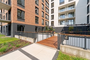 A modern apartment building with a wooden deck, metal railings, and a landscaped garden area. - Portowa Riverside Apartment (Kraków)
