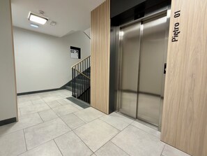 A modern elevator with a digital display, a staircase with black railings, and a sign indicating the floor number. - Madalińskiego Prime Studio 3B (Wrocław)