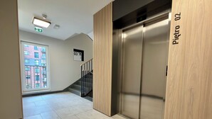 Ein moderner Aufzug mit digitaler Anzeige, eine Treppe mit Handlauf und ein Schild mit der Etagennummer.