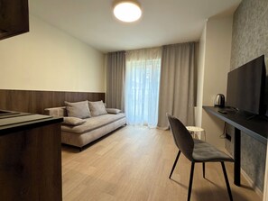 Een moderne hotelkamer met een bank, een televisie, een koffiezetapparaat en een bureau.