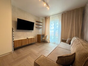 Ein modernes Wohnzimmer mit Flachbildfernseher an der Wand, einer Holz-Unterhaltungseinheit, einem Sofa und einem Sessel.