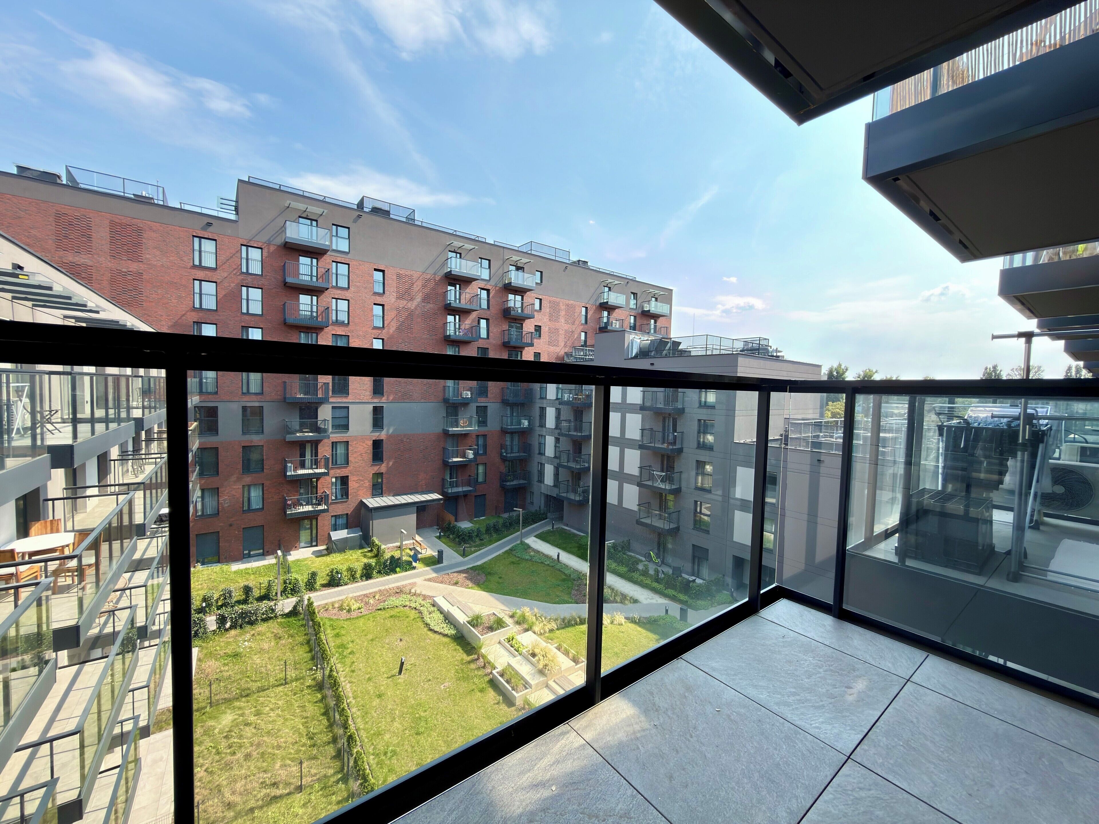 Een modern appartement met een glazen balkon met uitzicht op een binnentuin en omliggende gebouwen.
