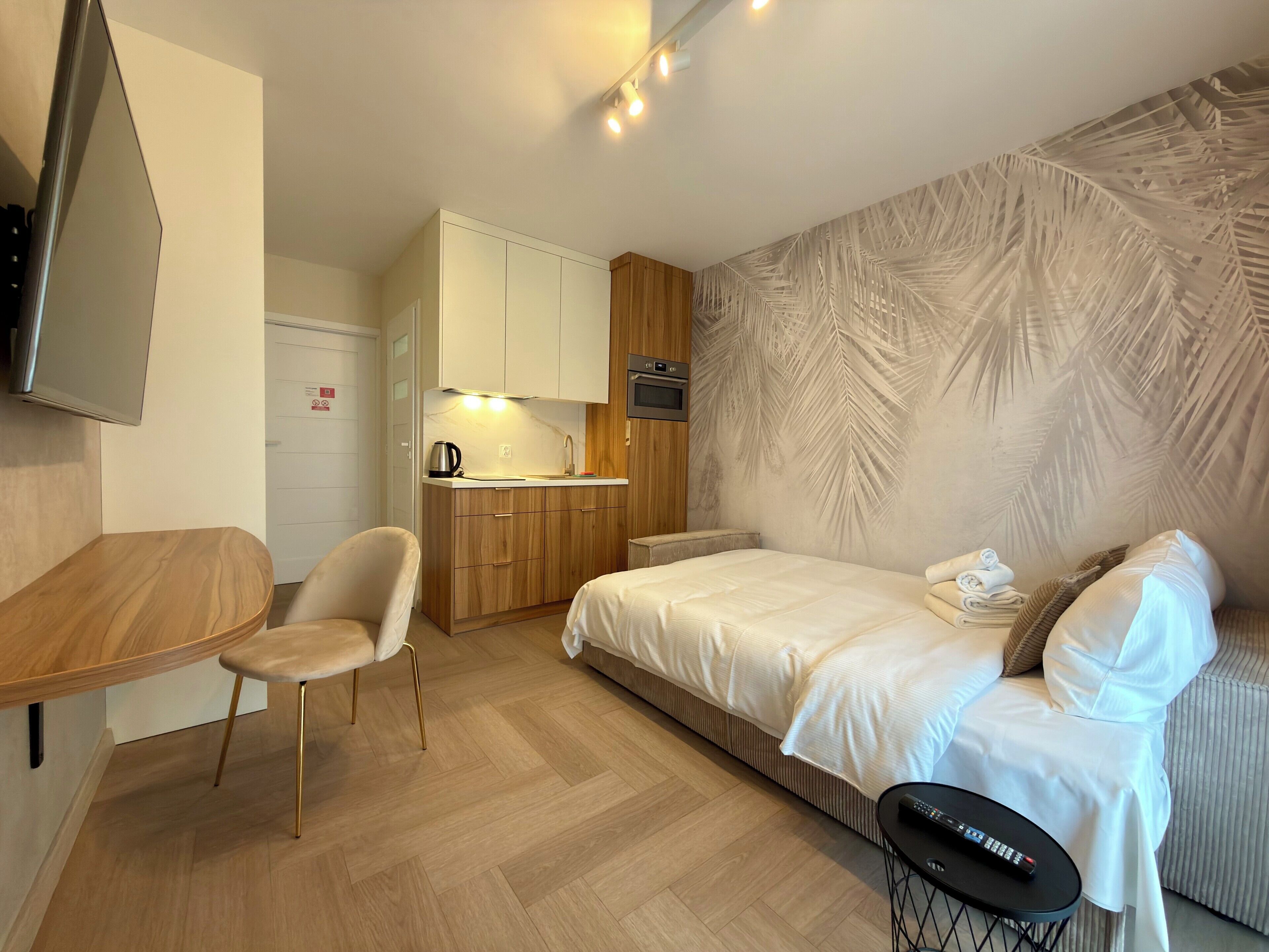 Une chambre d’hôtel compacte comprenant un coin cuisine, un lit, un espace salon et un téléviseur fixé au mur.