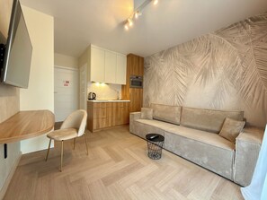Un espace de vie compact comprenant un coin cuisine, un canapé, un coin repas et un téléviseur fixé au mur.