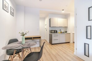A modern kitchen with white cabinets and a microwave, a dining area with a table and chairs, and a vase with flowers on the table. - Krzywa Harmony Apartment (Katowice)