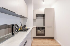A compact kitchen with a built-in oven, a microwave, and a stainless steel range hood. - Krzywa Harmony Apartment (Katowice)
