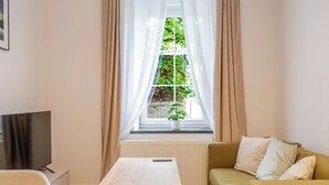 A living room with a sofa, a coffee table, a TV, and a window with curtains. - Krzywa Harmony Apartment (Katowice)
