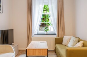 A living room with a sofa, a coffee table, a TV, and a window with curtains. - Krzywa Harmony Apartment (Katowice)