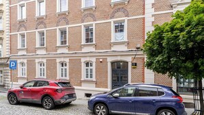 A red and a blue car parked in front of a brick building with multiple windows and a door. - Krzywa Harmony Apartment (Katowice)