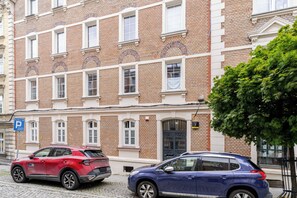 A red and a blue car parked in front of a brick building with multiple windows and a door. - Krzywa Harmony Apartment (Katowice)