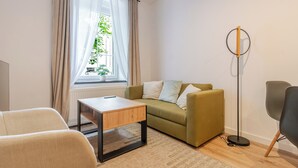 A modern living room with a sofa, a small table, a floor lamp, and a window with curtains. - Krzywa Harmony Apartment (Katowice)