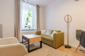 A modern living room with a sofa, a small table, a floor lamp, and a window with curtains. - Krzywa Harmony Apartment (Katowice)