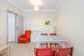 A compact room with a dining table, red chairs, a white cabinet, and a door. - Powstańców Central Apartment (Katowice)