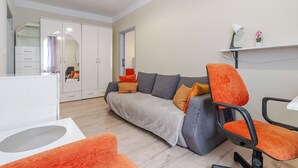Ett modernt vardagsrum med en grå soffa, orange fåtöljer, ett vitt skrivbord och en stor garderob med en spegel.