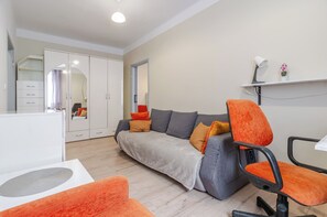 A modern living room with a grey sofa, orange armchairs, a white desk, and a large wardrobe with a mirror. - Powstańców Central Apartment (Katowice)