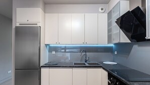 Una cocina moderna con refrigerador de acero inoxidable, gabinetes blancos, encimera negra e iluminación debajo de los gabinetes.