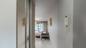 Un pasillo que conduce a un dormitorio con una cama, una mesita de noche, una lámpara y un teléfono.
