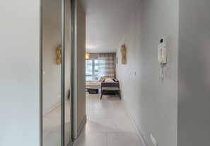 A hallway leading to a bedroom with a bed, a bedside table, a lamp, and a telephone. - Warszawska Chic Apartment (Rzeszów)