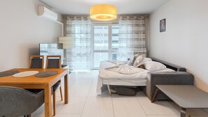 Un espacio habitable moderno y funcional con comedor, una cama y un banco, y un ventanal con cortinas.