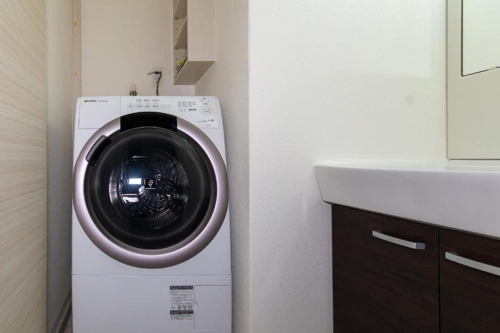 A front-loading washing machine in a laundry room with a white wall and a wooden cabinet.