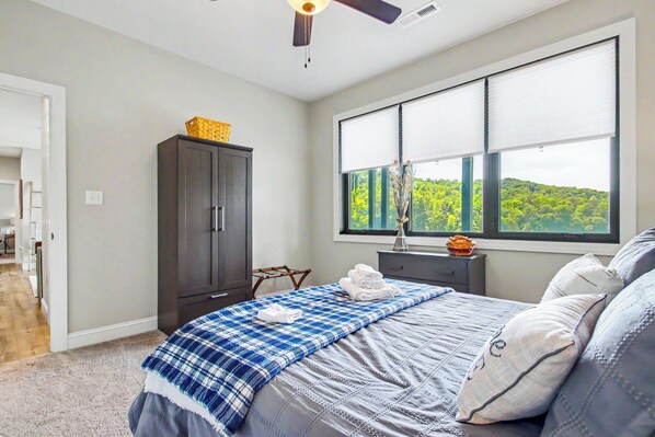 A bedroom with a bed, a wardrobe, a window with a view, and a ceiling fan.
