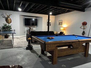 A pool table with balls, a television, a sofa, and a decorative deer head.